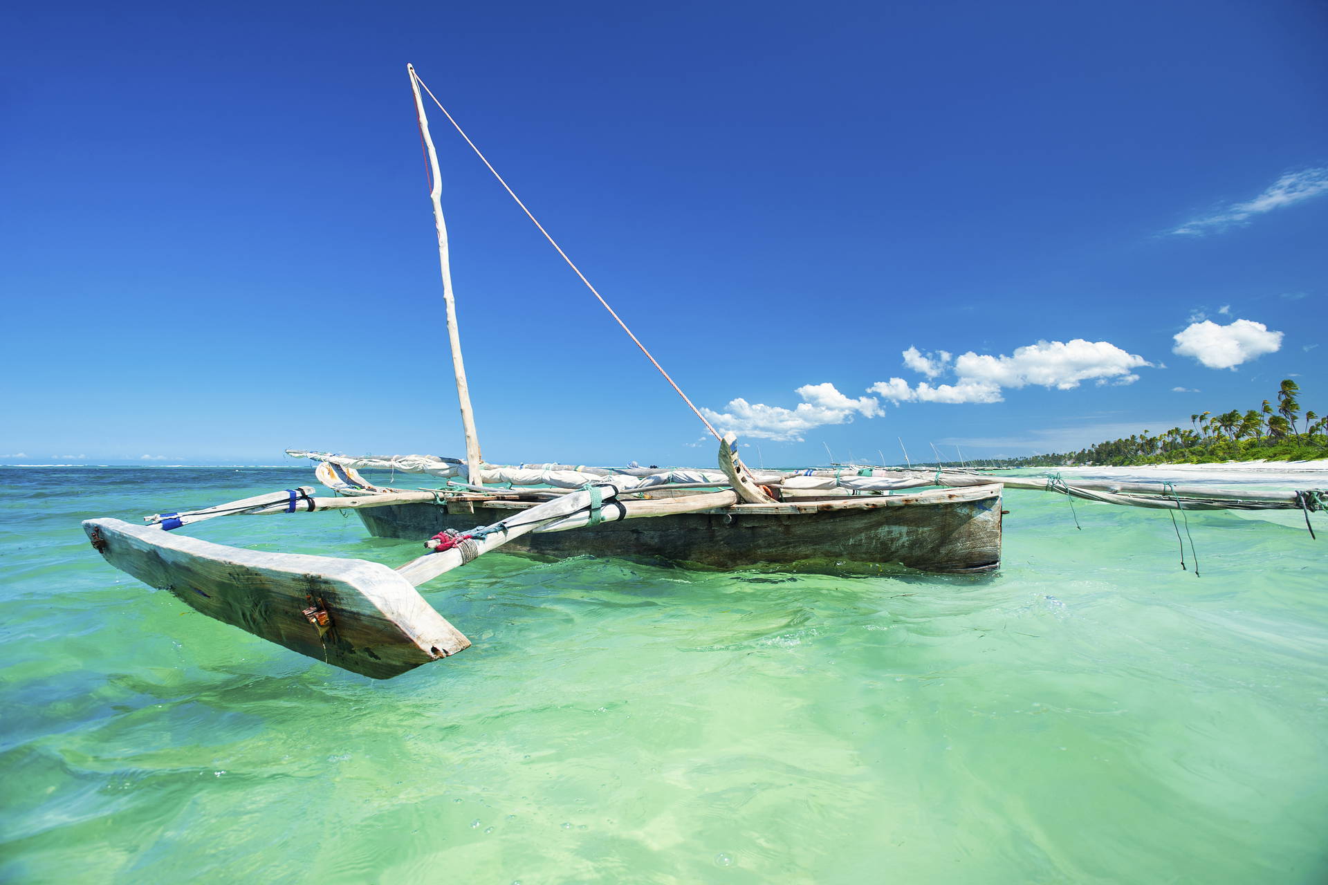 Drewniana łódka z żaglem na turkusowej wodzie.