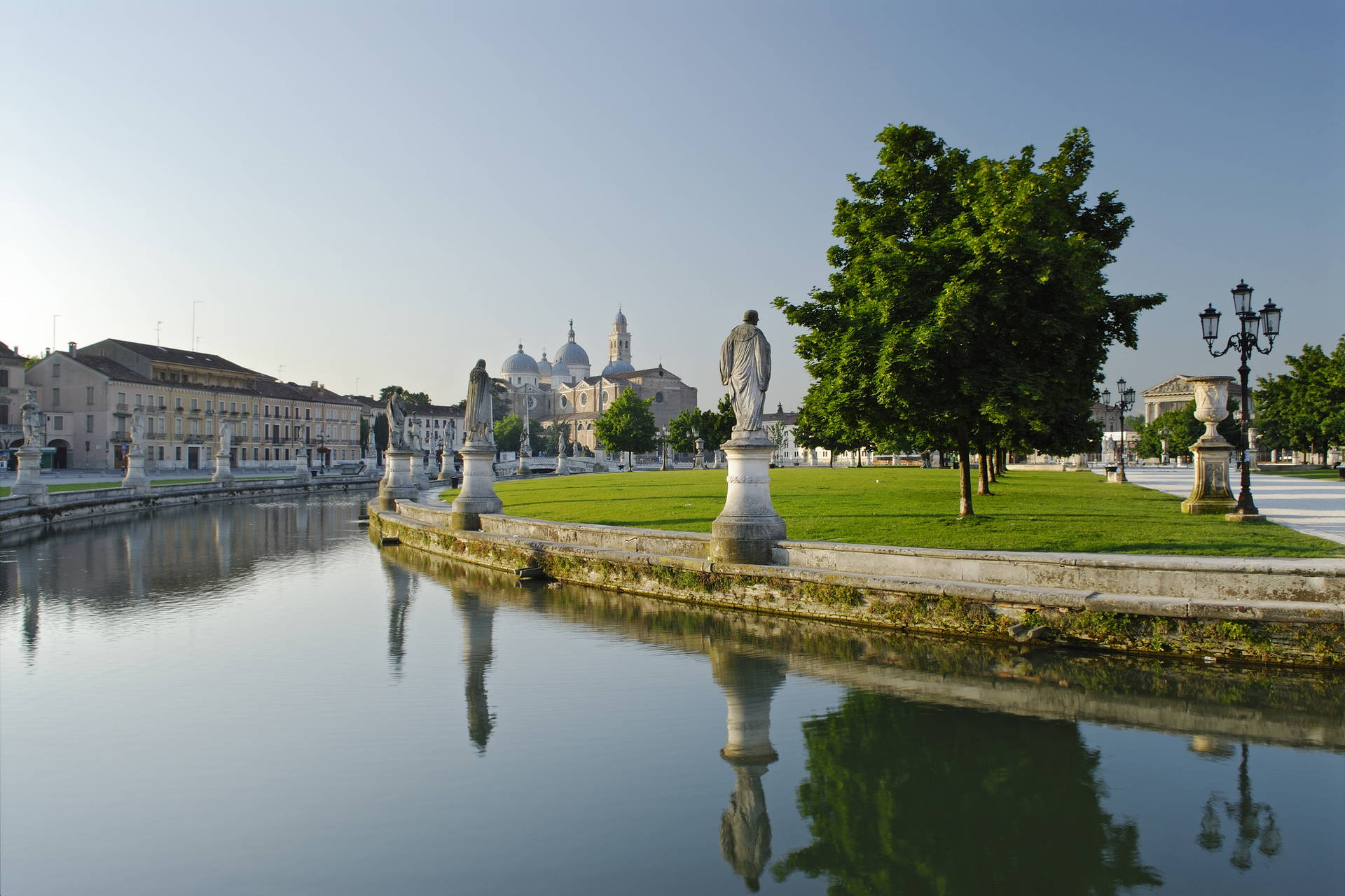 Prato della Valle w Padwie z bazyliką św. Justyny w tle. W parku znajduje się kanał z rzeźbami po bokach.