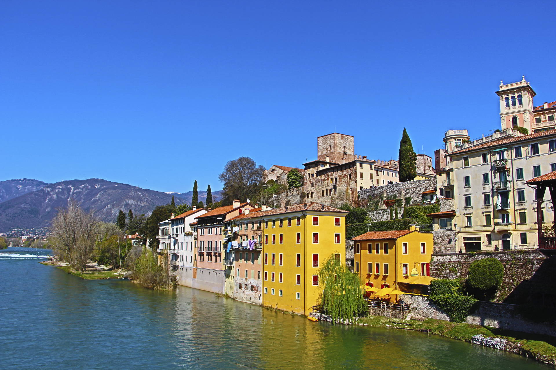 Kolorowe budynki w Bassano del Grappa we Włoszech nad rzeką, w tle wzgórza.