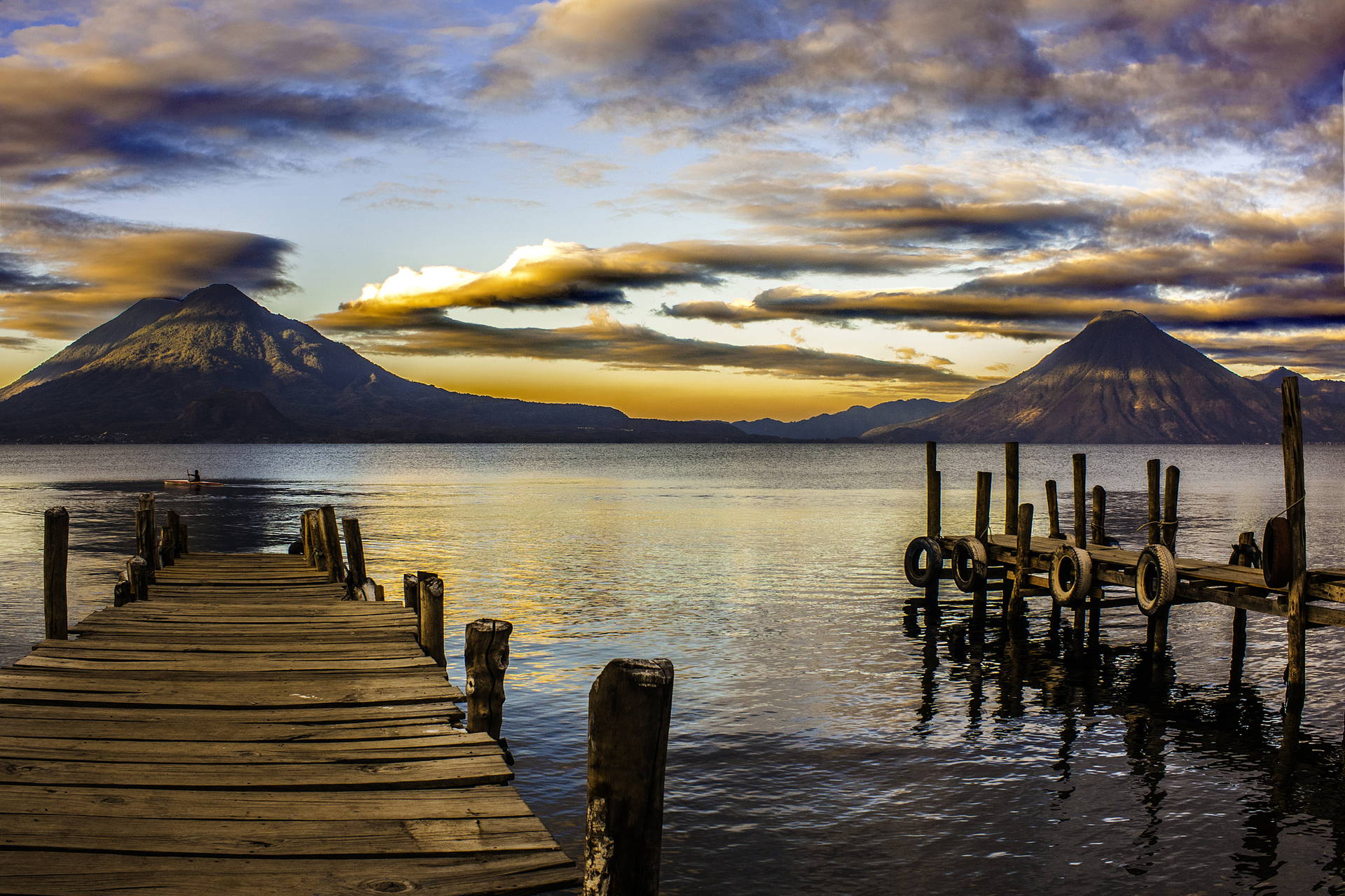 Jezioro Atitlán z drewnianymi pomostami na pierwszym planie i wulkanami w tle.