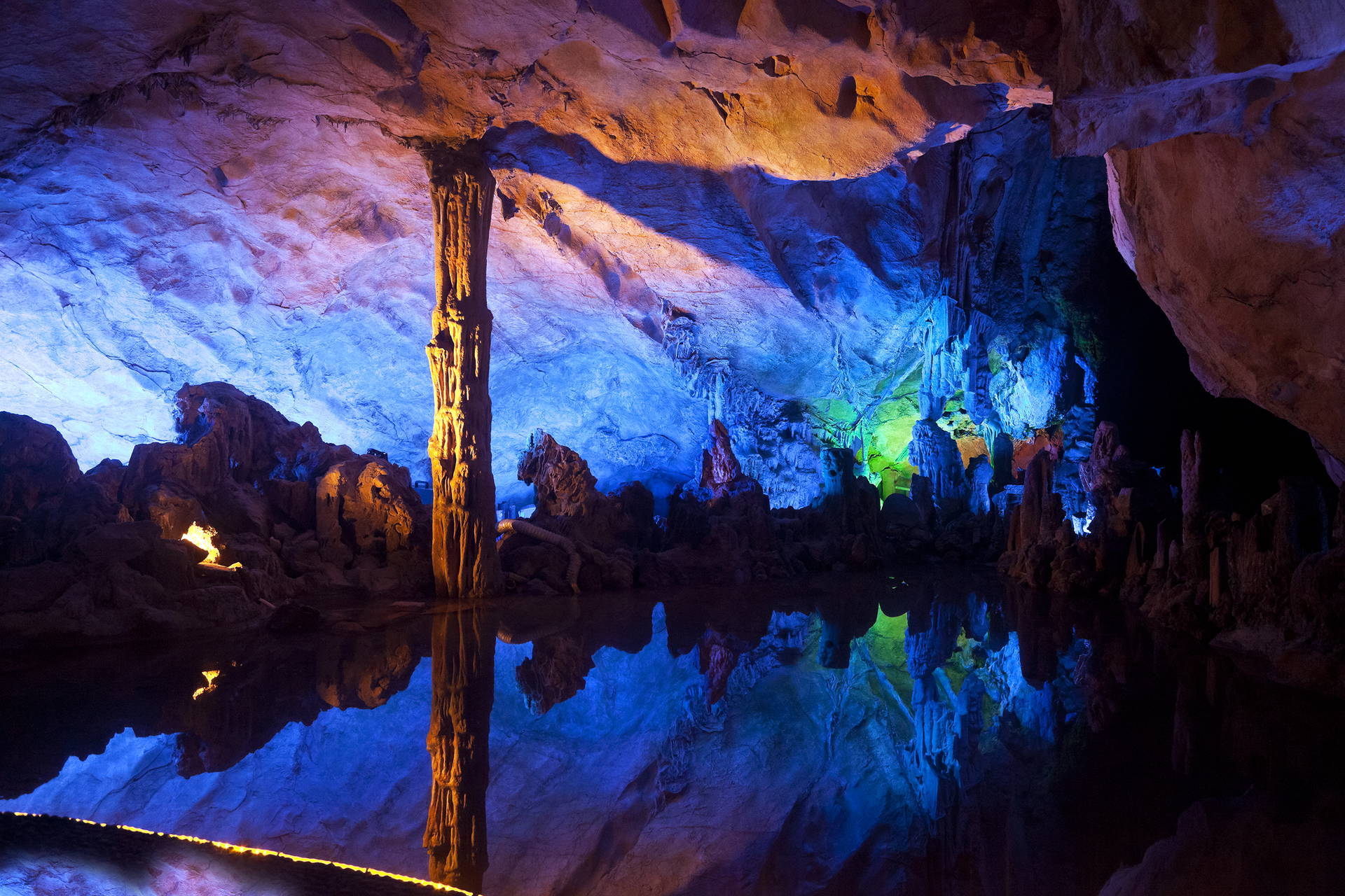 Kolorowe stalaktyty i stalagmity odbijają się w wodzie jaskini.