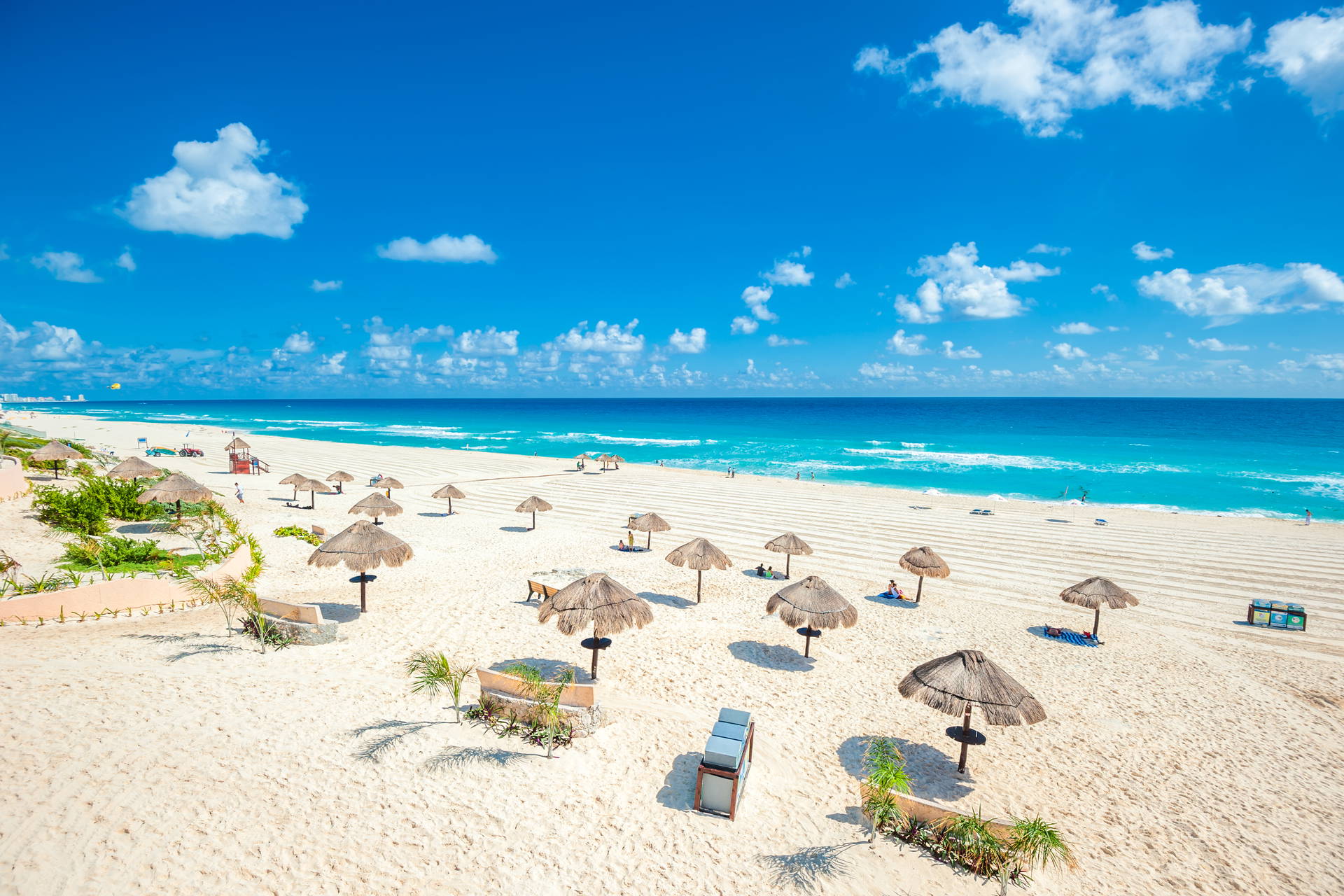 Plaża w Cancun z parasolami, błękitnym niebem i morzem w tle.