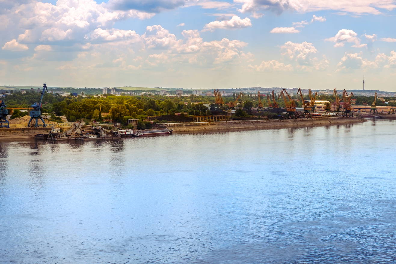 Panorama rzeki z dźwigami portowymi i zabudową miejską w tle.