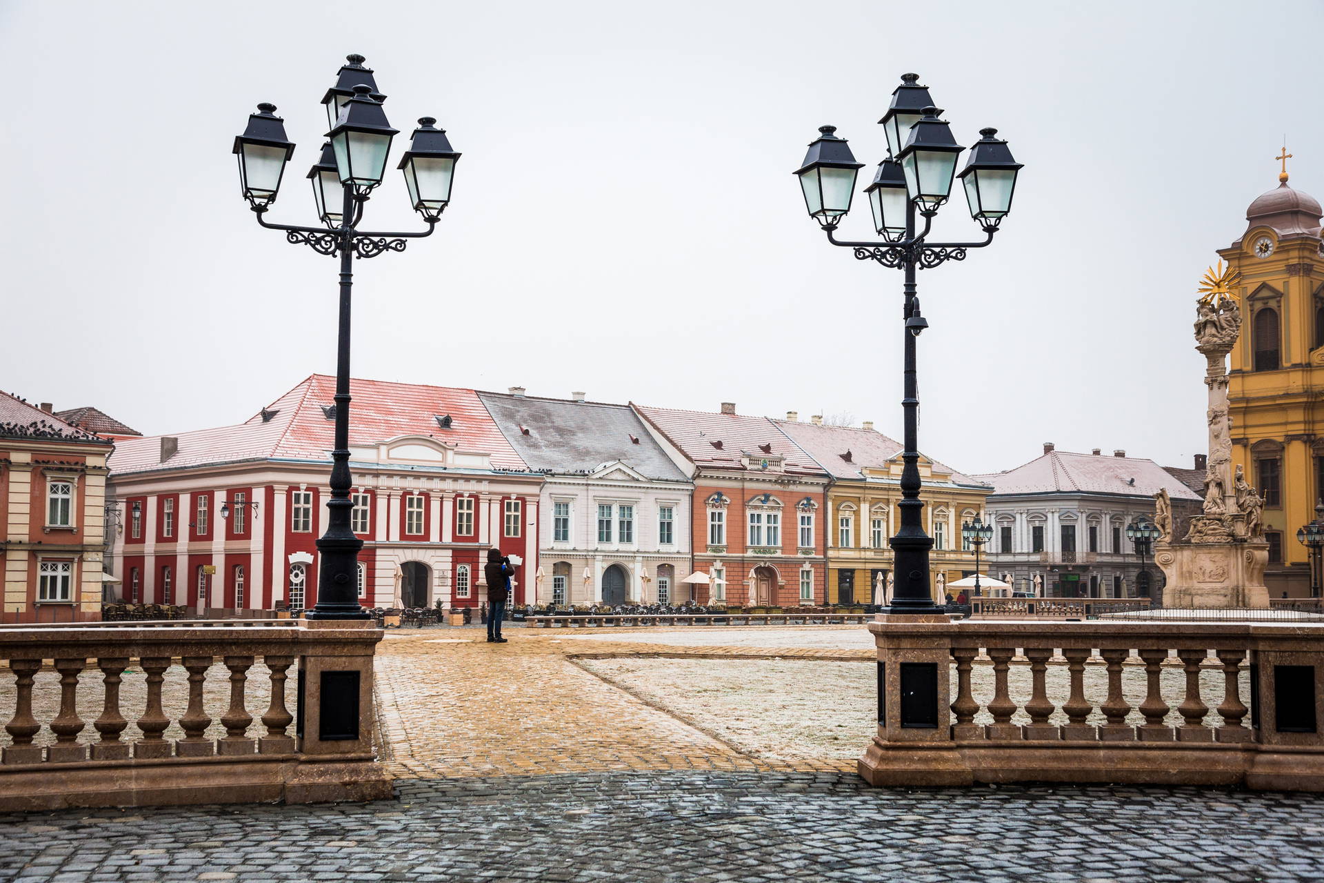 Plac z brukowaną nawierzchnią, budynkami w tle i wysokimi, czarnymi latarniami.