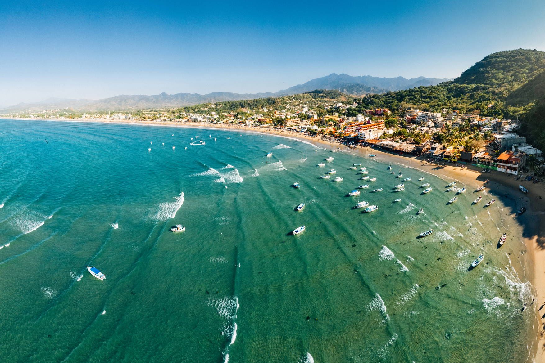 Panorama plaży Sayulita w Meksyku. Na wodzie łodzie, w tle góry.