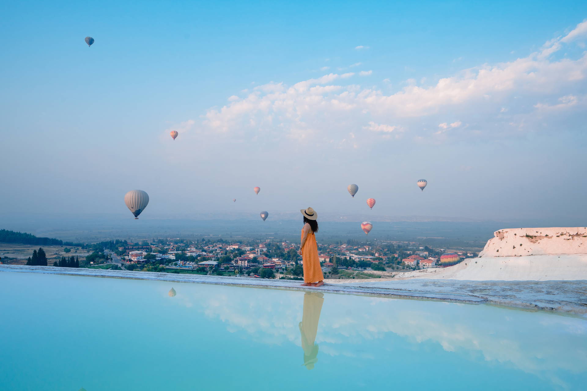 Kobieta na tarasach Pamukkale obserwuje balony unoszące się nad doliną o wschodzie słońca.
