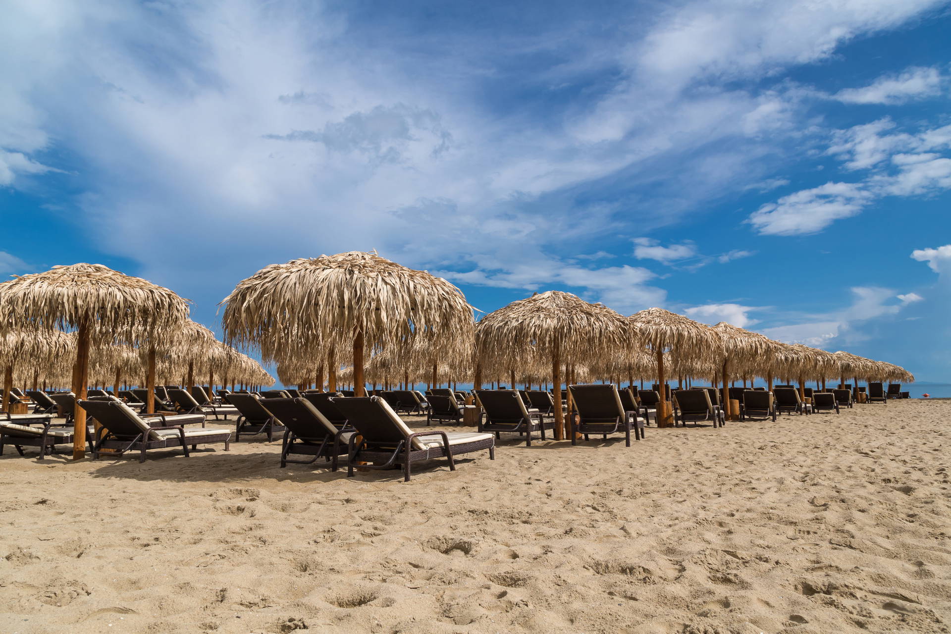 Plaża z leżakami pod słomianymi parasolami.