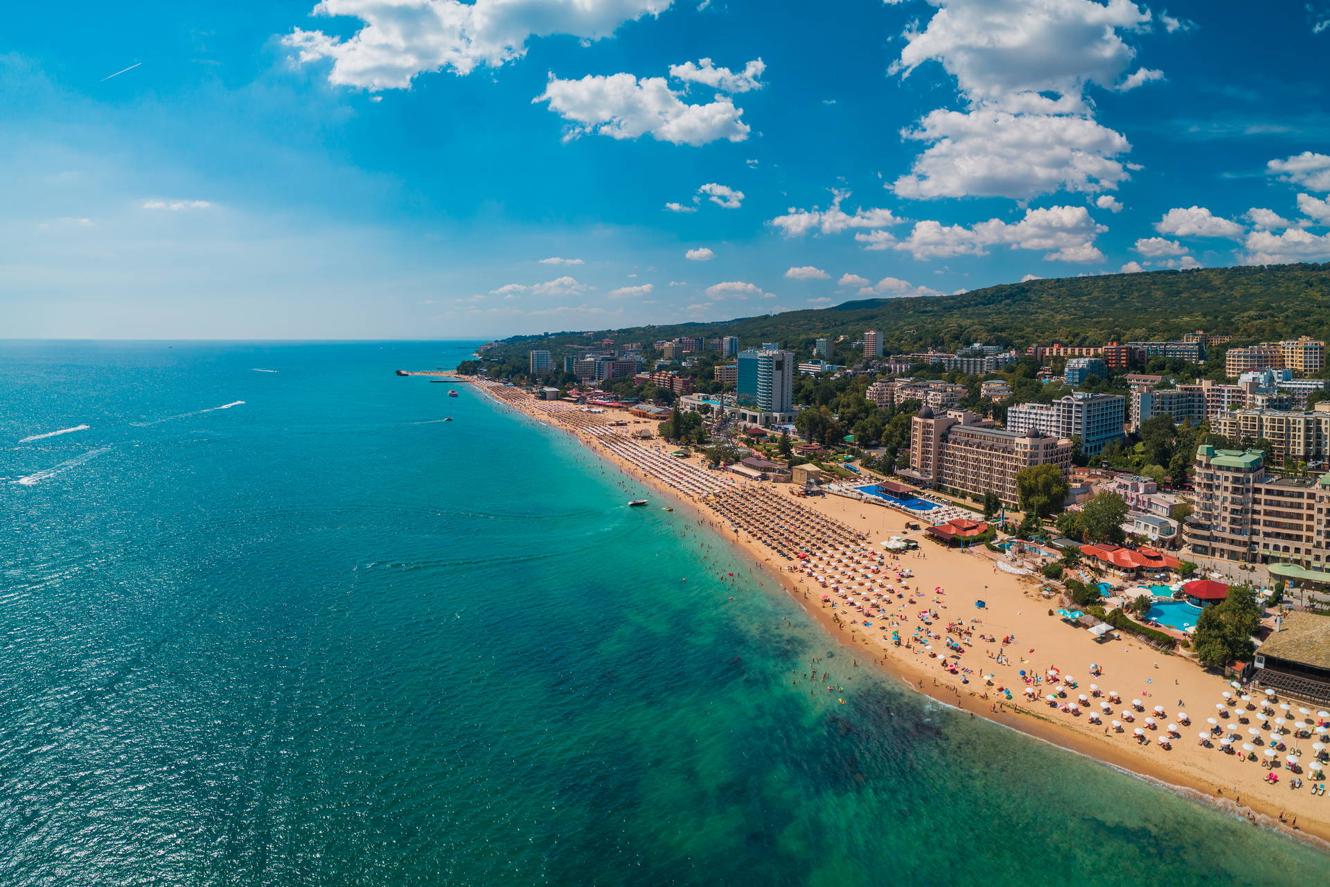 Widok z lotu ptaka na Złote Piaski w Bułgarii: piaszczysta plaża, hotele i turyści nad turkusowym morzem.