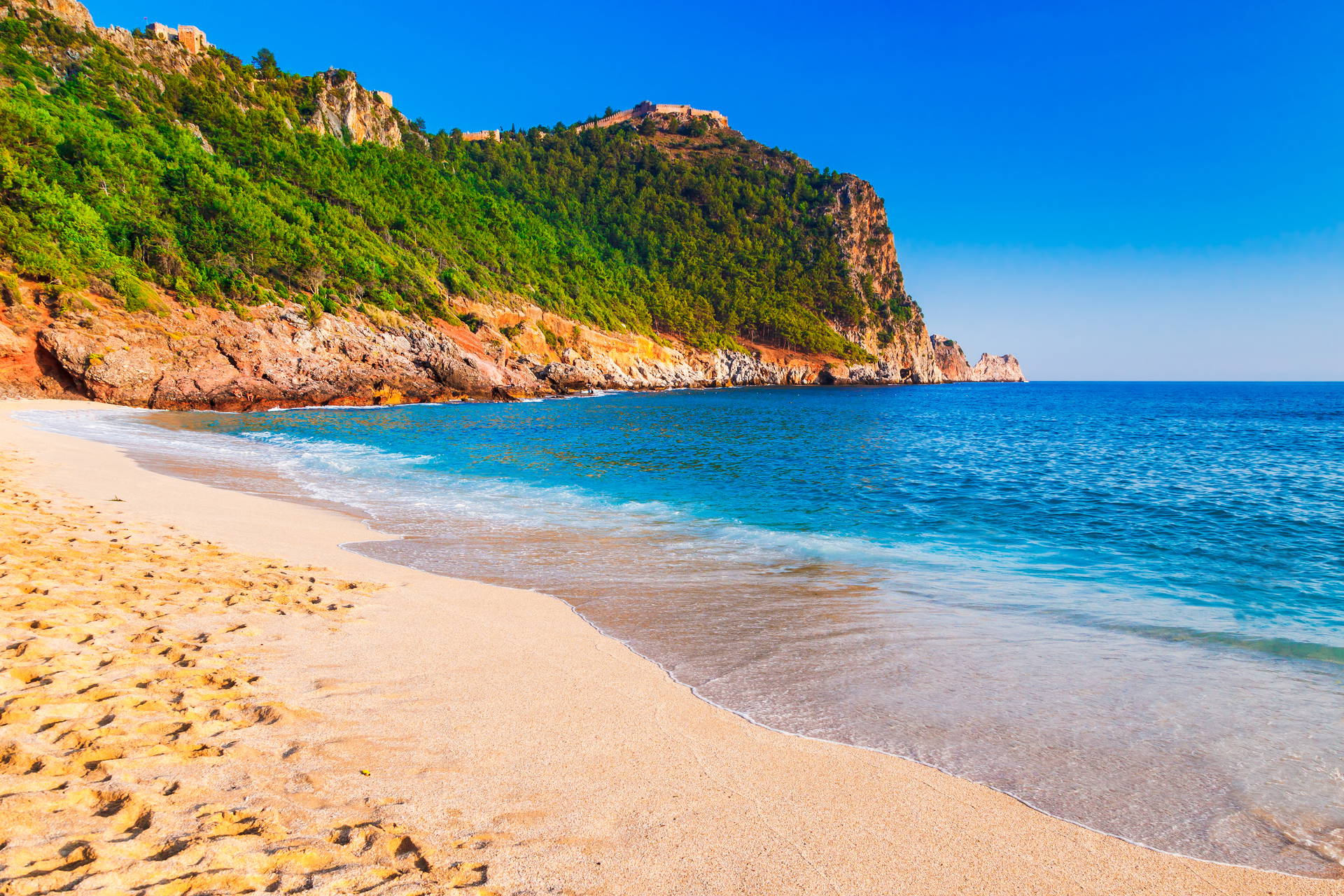 Plaża Kleopatry w Alanyi z klifem i zamkiem w tle.