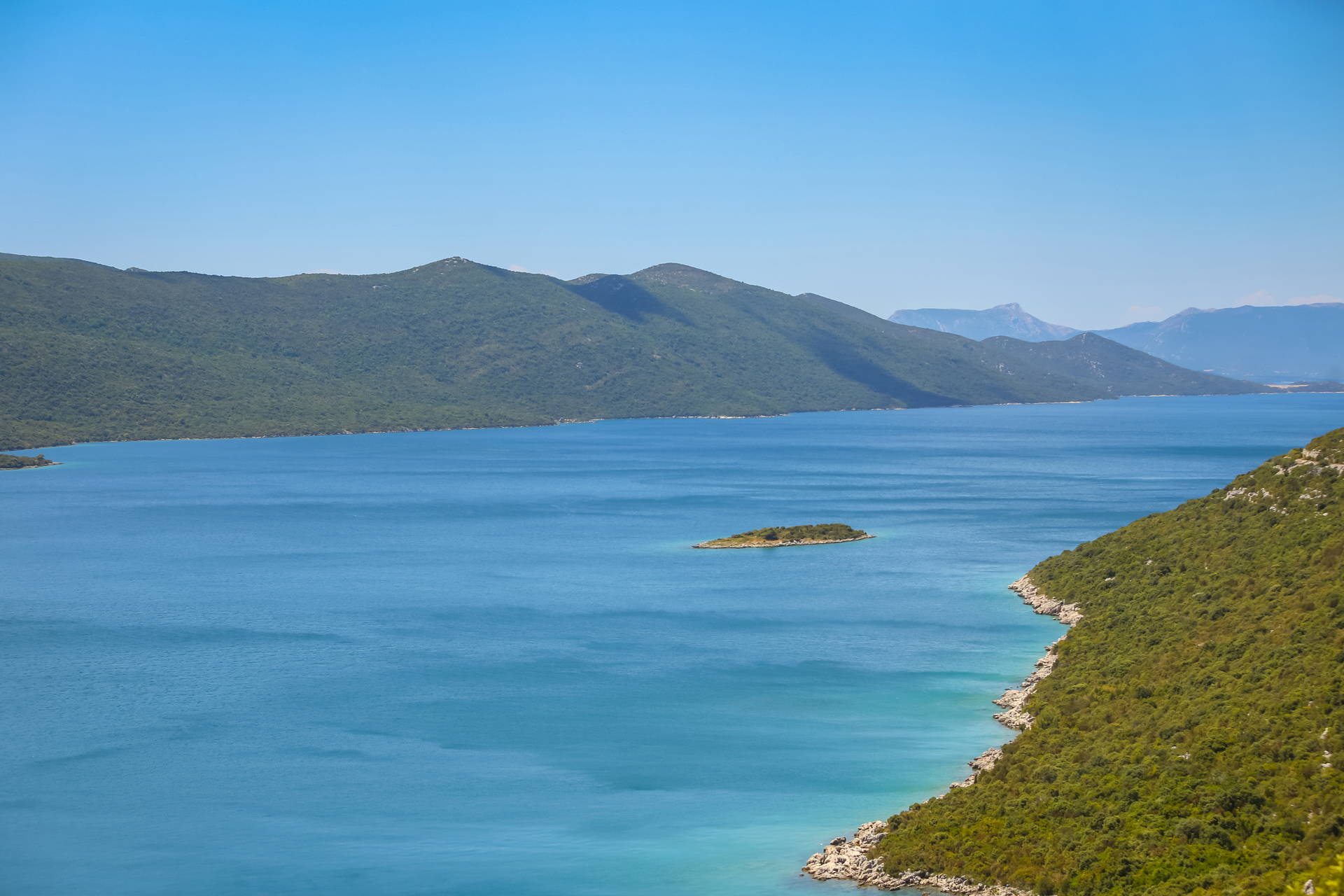 Krajobraz morski z wyspą i górami w oddali.