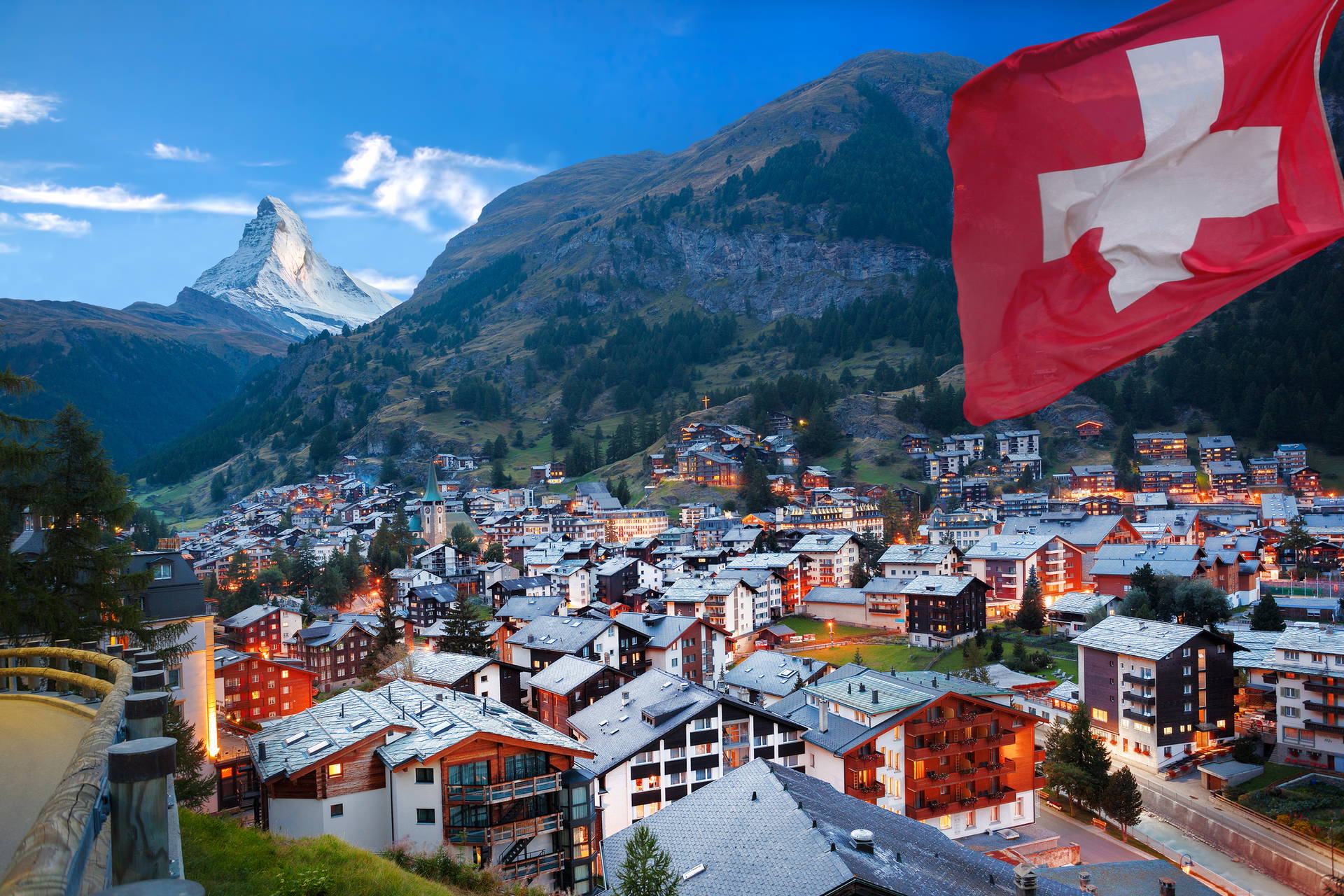 Panorama Zermatt z flagą Szwajcarii na pierwszym planie i Matterhornem w tle.