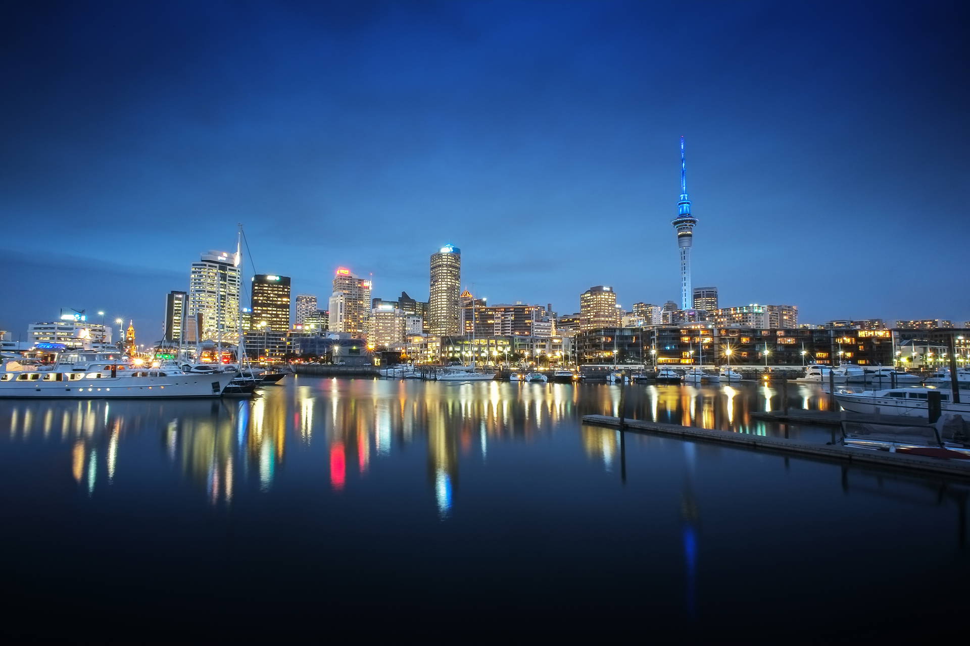 Panorama nocna Auckland z wieżą Sky Tower i jachtami w porcie.