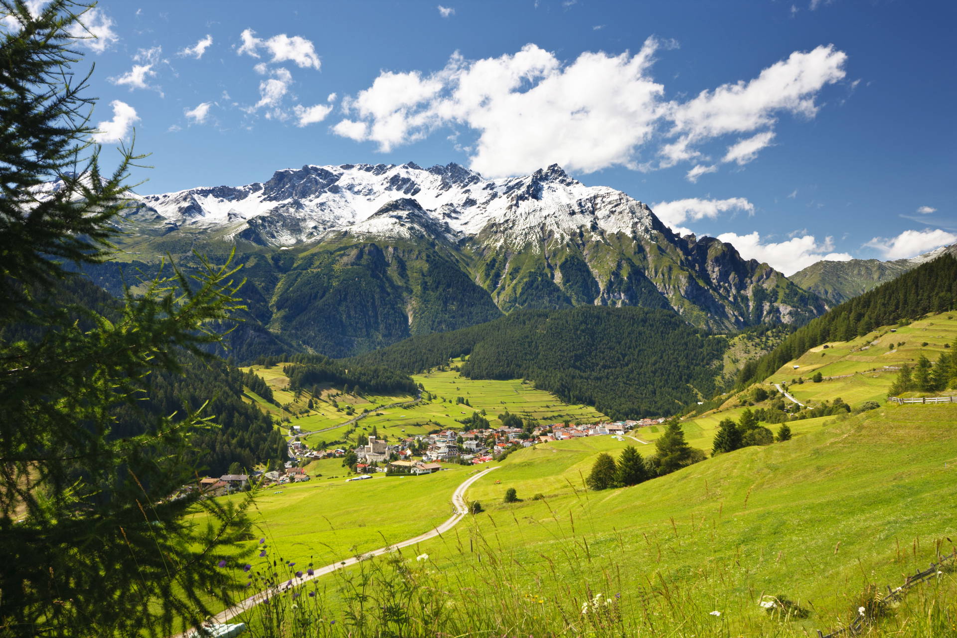 Górski krajobraz z wioską w dolinie i ośnieżonymi szczytami.