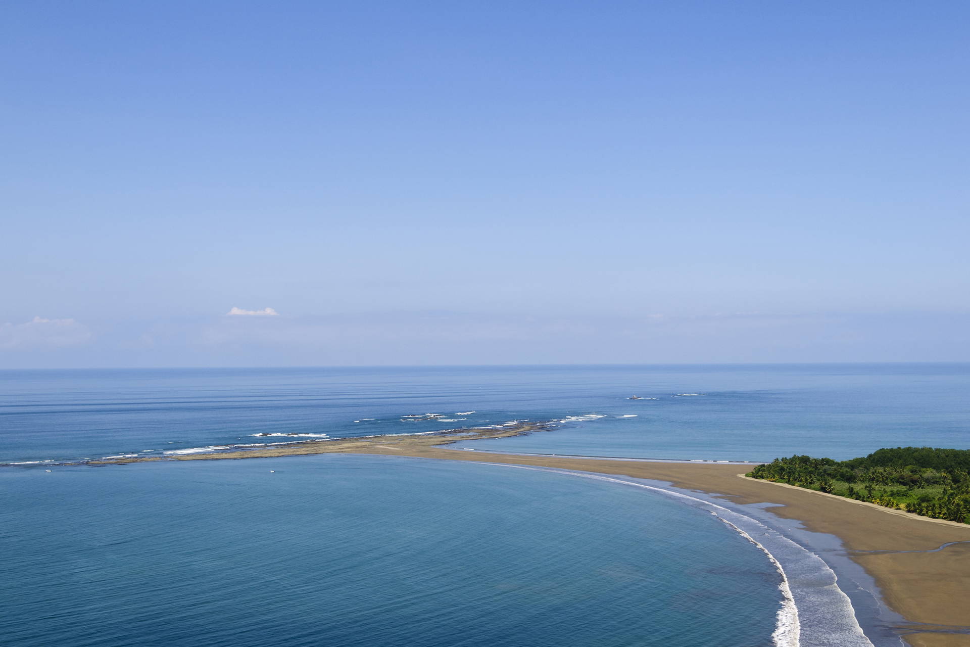Długa, piaszczysta plaża i błękitna woda widziane z góry.