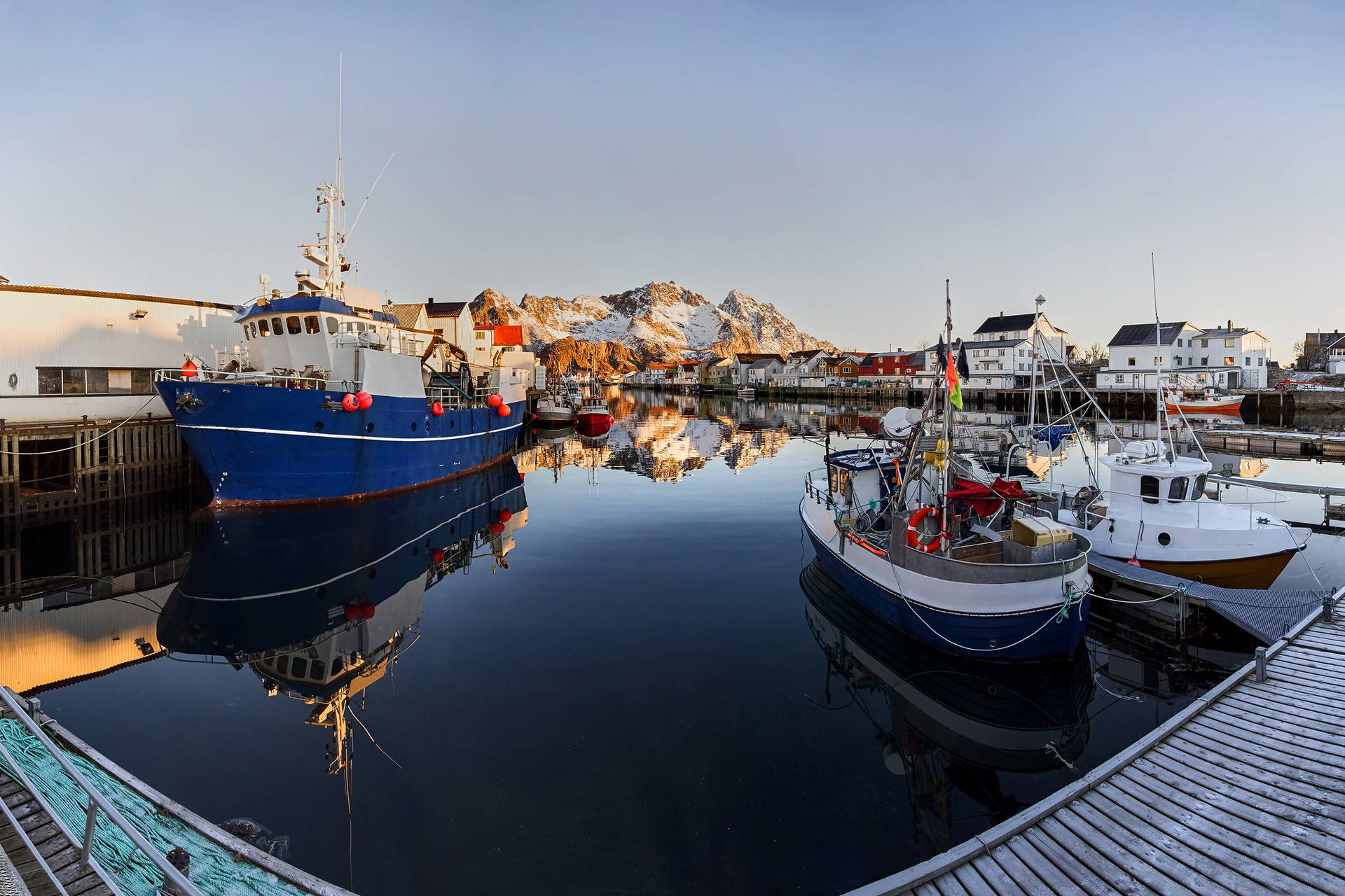 Port w Norwegii z łodziami rybackimi na wodzie i górami w tle.