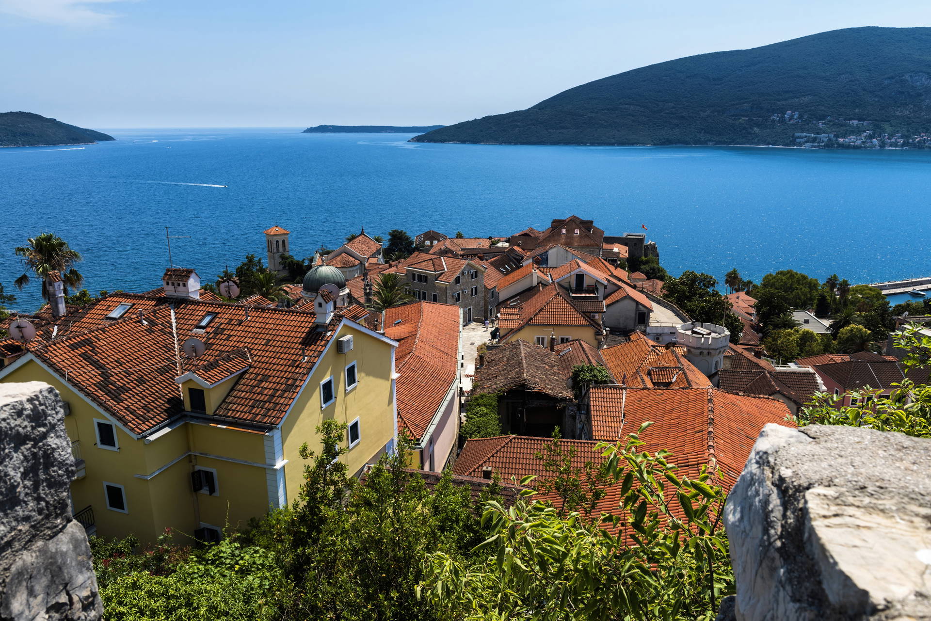 Perast w Czarnogórze z czerwonymi dachami budynków i błękitnym morzem w tle.