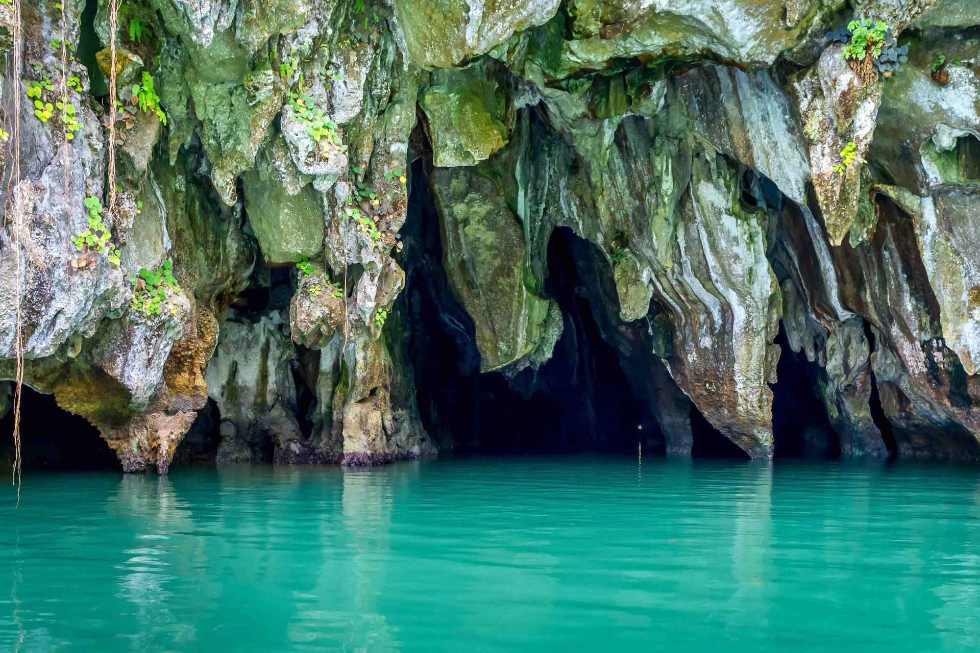 Park Narodowy Rzeki Podziemnej Puerto Princesa. Turkusowa woda wpływa do skalistej jaskini otoczonej zielenią.