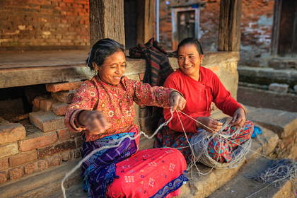 Dwie uśmiechnięte kobiety w Nepalu pracują z włóczką na werandzie.