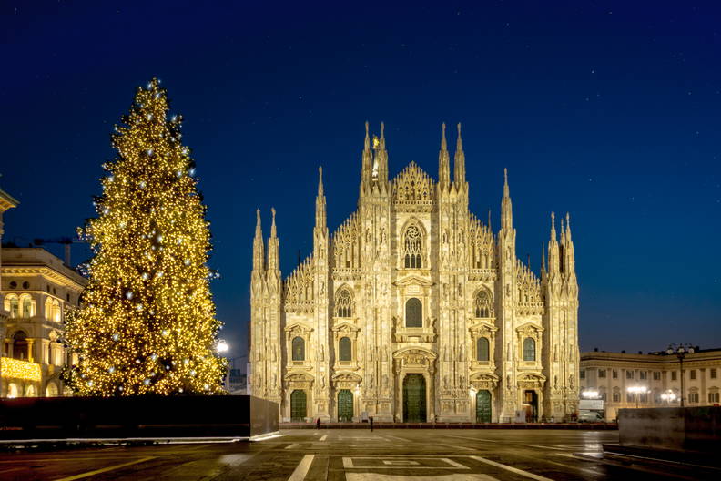 Oświetlona nocą Katedra Duomo w Mediolanie z dużą, rozświetloną choinką.