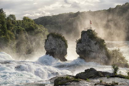 Rheinfall, wodospad w Szwajcarii ze szwajcarską flagą powiewającą na skale.