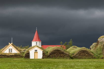 Panorama islandzkiej osady Keldur z budynkami krytymi darnią i kościołem. W tle pochmurne niebo.