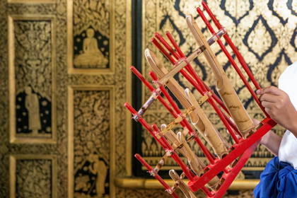 Osoba trzyma instrument angklung na tle zdobionej ściany.