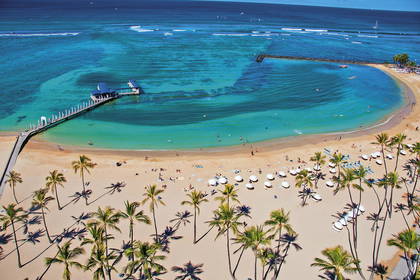 Widok z góry na plażę Waikiki z palmami, turkusową wodą i molo.
