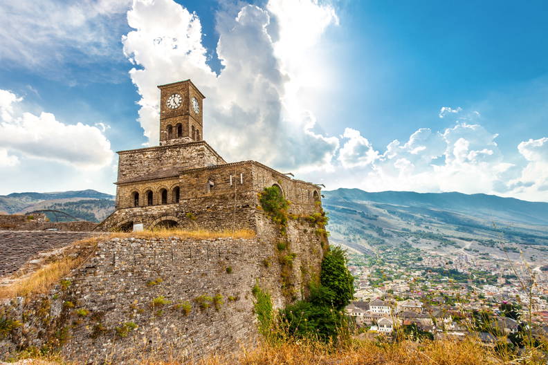 Zamek w Gjirokastrze z wieżą zegarową. W tle widok na miasto i góry.