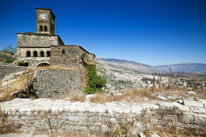 Zamek w Gjirokastrze z wieżą zegarową. W tle widok na miasto i góry.