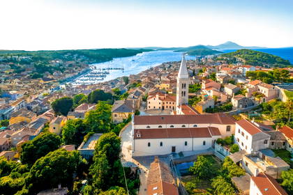 Widok z lotu ptaka na Mali Lošinj w Chorwacji. W centrum miasteczka widać kościół, a poniżej port nad błękitnym morzem.