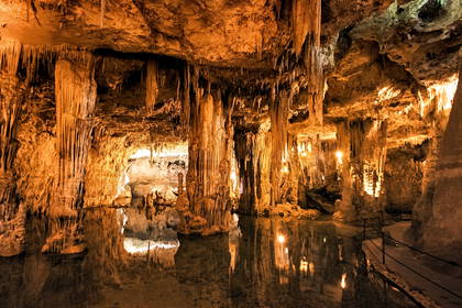 Jaskinia ze stalaktytami i stalagmitami odbijającymi się w wodzie.
