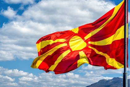 Flaga Macedonii Północnej powiewająca na tle błękitnego nieba z białymi chmurami.