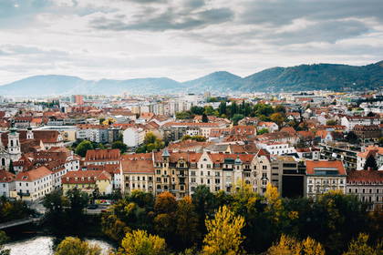Panorama miasta Graz w Austrii z budynkami na pierwszym planie i górami w tle.