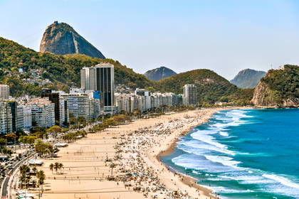 Zatłoczona plaża Copacabana w Rio de Janeiro z górą Głowa Cukru w tle.