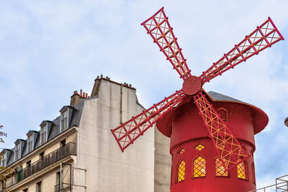 Wiatrak Moulin Rouge na tle budynku w Paryżu.