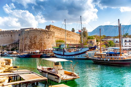 Port w Kyrenii z zamkiem i łodziami zacumowanymi przy nabrzeżu.