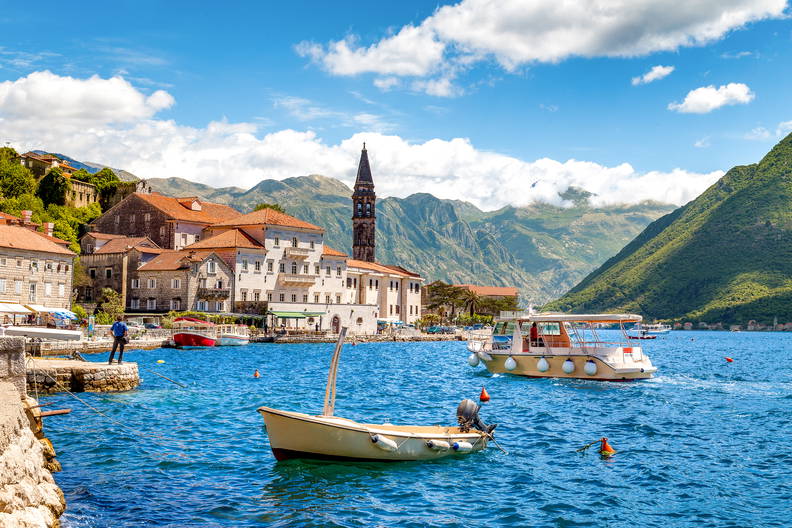 Widok na miasto Perast w Czarnogórze. Po błękitnych wodach Zatoki Kotorskiej pływają łodzie na tle gór.