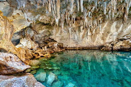 Turkusowa woda w jaskini ze stalaktytami i stalagmitami.