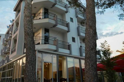 Hotel z balkonami widoczny zza drzew.