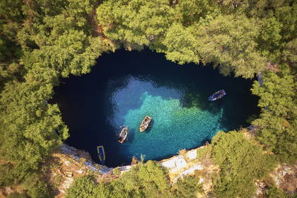 Jezioro Melissani na Kefalonii w Grecji z lotu ptaka. Wokół jeziora rosną drzewa, a na wodzie pływają łodzie.