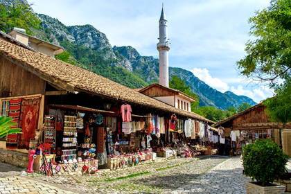 Stary Bazar w Krui w Albanii. Brukowaną uliczkę wypełniają stragany z pamiątkami, a w tle widać minaret i góry.