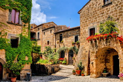 Uliczka w Civita di Bagnoregio z kamiennymi budynkami ozdobionymi kwiatami.