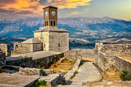Zamek w Gjirokastrze i wieża zegarowa na tle gór.