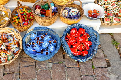 Na pierwszym planie widać niebieskie i czerwone, zdobione kubki ceramiczne, a w tle inne pamiątki w wiklinowych koszach.