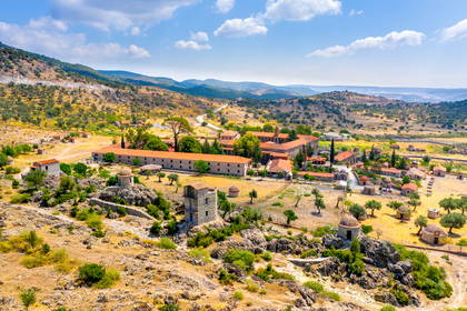 Widok z lotu ptaka na klasztor św. Jana Teologa na Lesbos. Kamienne budynki z czerwoną dachówką stoją pośród zielonych wzgórz.