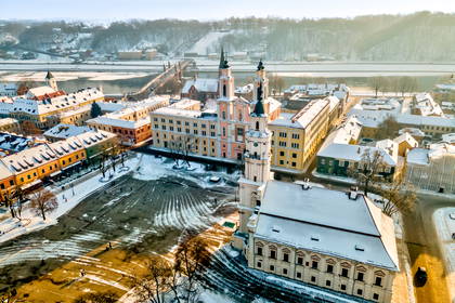 Widok z lotu ptaka na ośnieżony plac Ratuszowy w Kownie z Ratuszem w centrum i barokowym kościołem tuż obok.