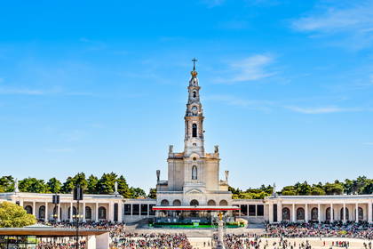 Bazylika Matki Boskiej Różańcowej w Fatimie z wieżą i zgromadzonym tłumem ludzi.