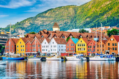 Bryggen w Bergen, Norwegia. Kolorowe budynki nad wodą, łodzie i góra w tle.