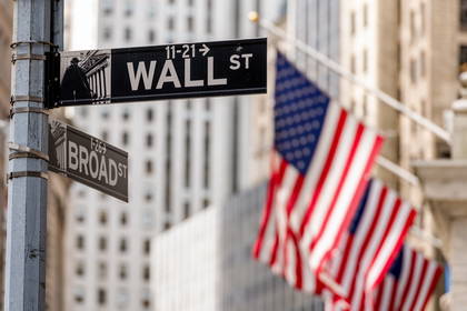 Znak uliczny Wall Street na tle flag USA.