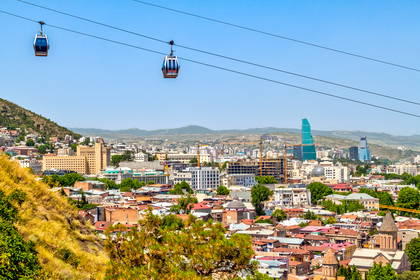 Widok z kolejki linowej na panoramę Tbilisi: stare miasto, nowoczesne wieżowce oraz góry w tle.